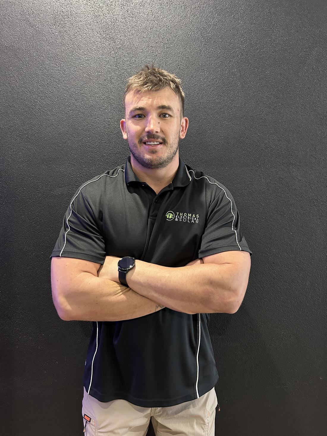 Bryce from Thomas Electrical and Solar, smiling with arms crossed in a black company polo
