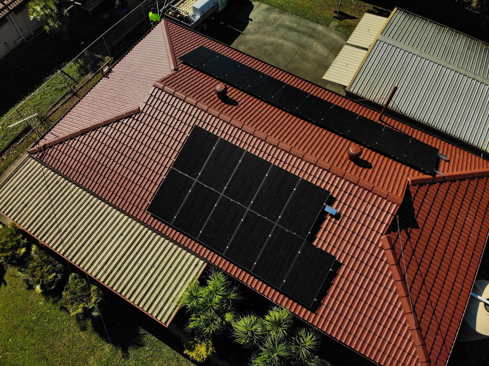 Aerial view of black solar panels installed across a red tile roof