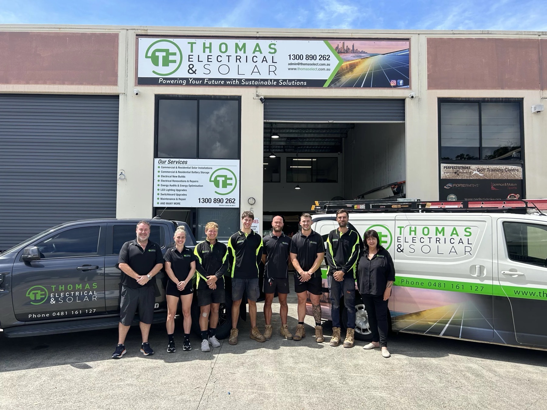 The Thomas Electrical and Solar team of eight standing in front of their Gold Coast headquarters with branded vehicles